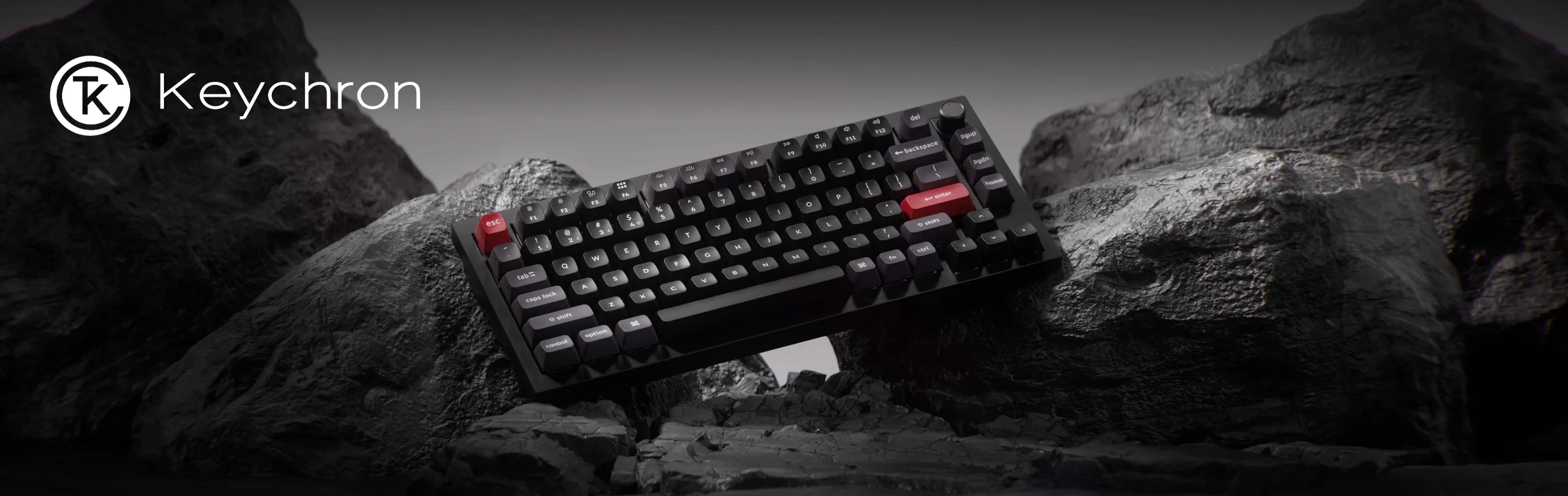 Clavier mécanique Keychron avec touches noires et touches Esc et Enter rouges sur des rochers sous le logo Keychron