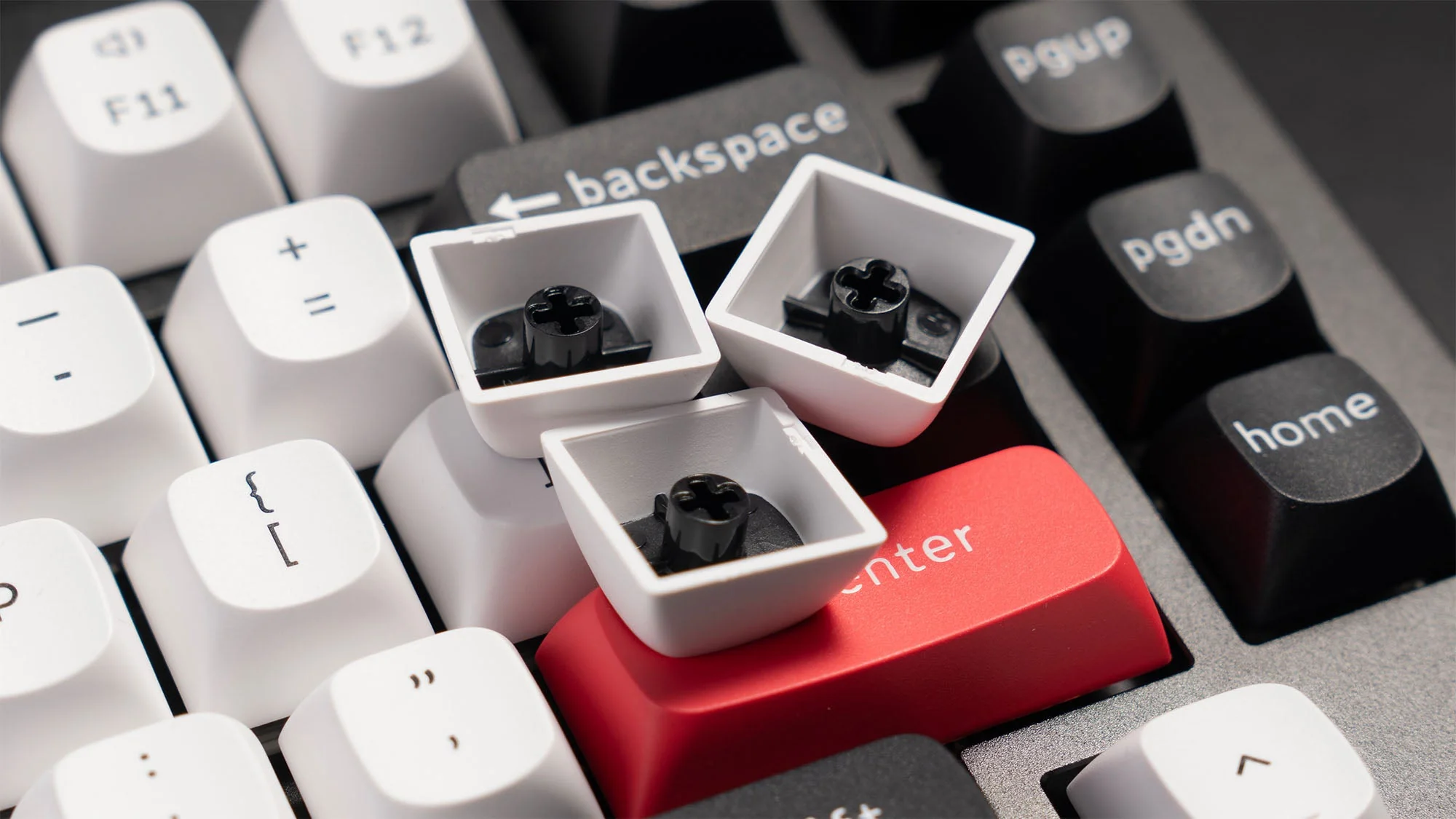 Gros plan d'un clavier Keychron avec keycaps blancs retirés montrant les sockets hot-swap et la touche Enter rouge