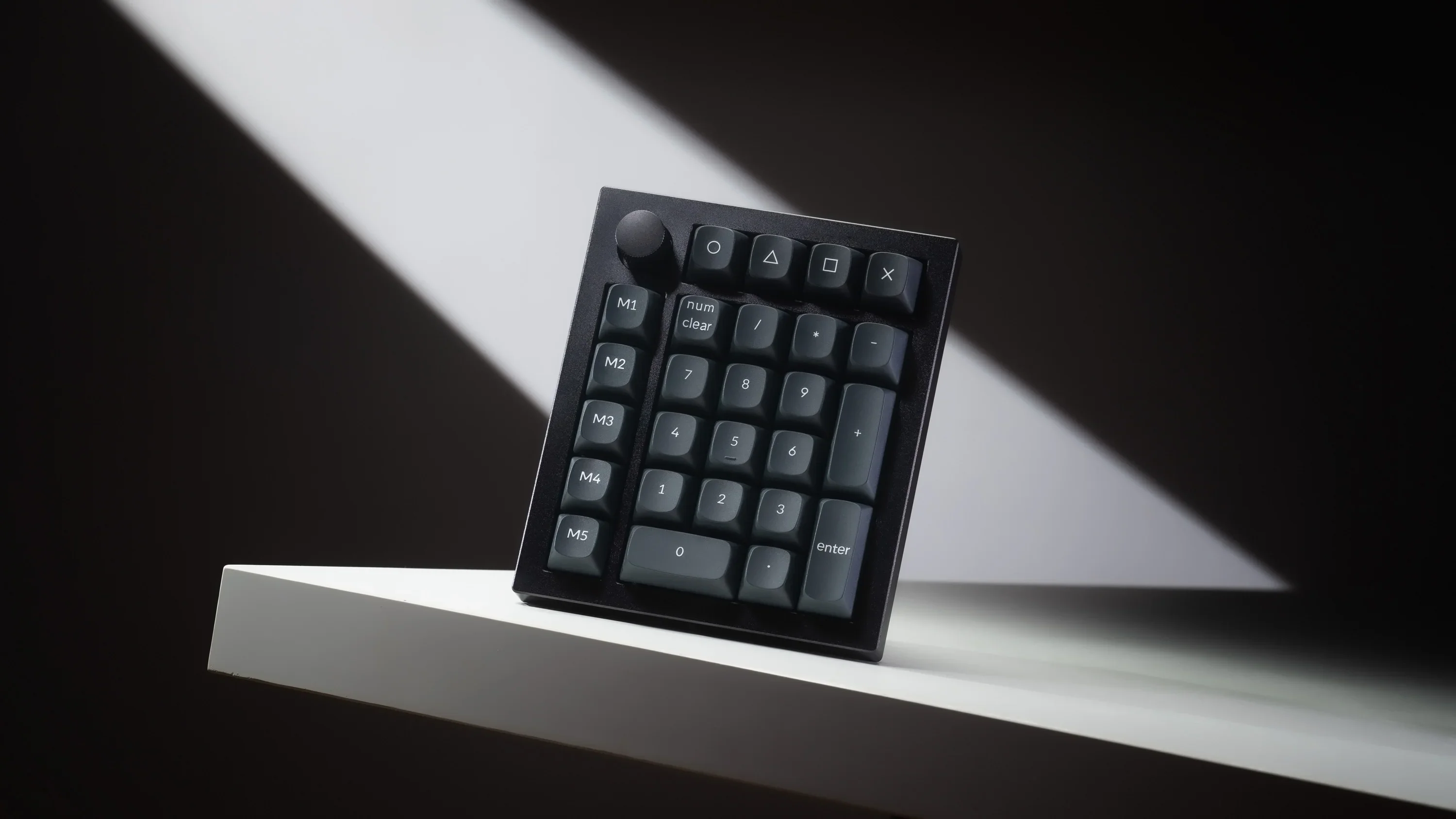Numpad mécanique noir Keychron avec molette, touches macro et touches chiffres sur une étagère blanche