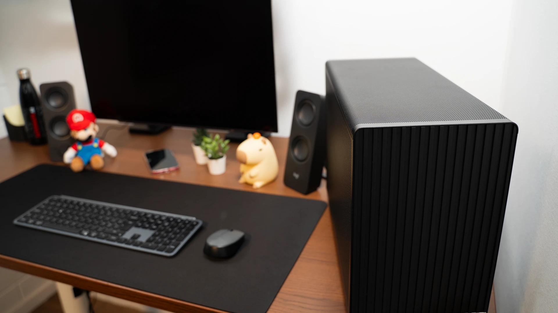 PC compact noir avec panneau avant en bois à côté d'un moniteur